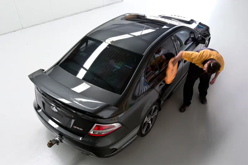 Auto body technician hand polishing the side of vehicle following car spray painting