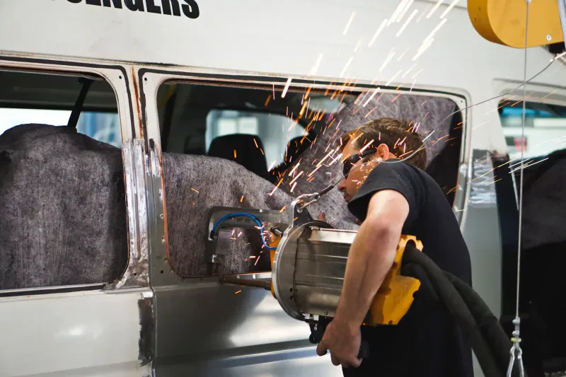 Auto body technician wearing safety glasses while repairing the side panel of a van with sparks flying